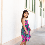 little girl with brown hair wearing a smocked spaghetti strap dress with fern and ginger print