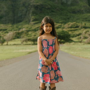 little girl wearing a navy spaghetti strap dress with bright pink hibiscus print
