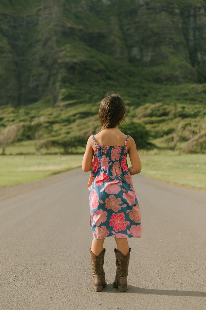 little girl wearing a navy spaghetti strap dress with bright pink hibiscus print