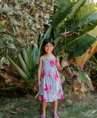 Girl wearing sleeveless dress with large pink floral print on lavender ground.