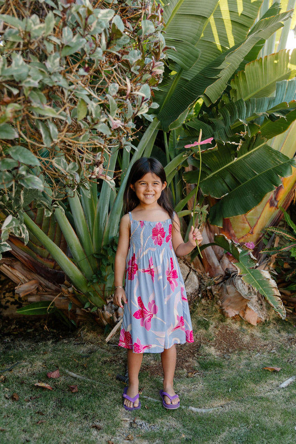 Girl wearing sleeveless dress with large pink floral print on lavender ground.