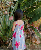 Girl wearing sleeveless dress with large pink floral print on lavender ground.