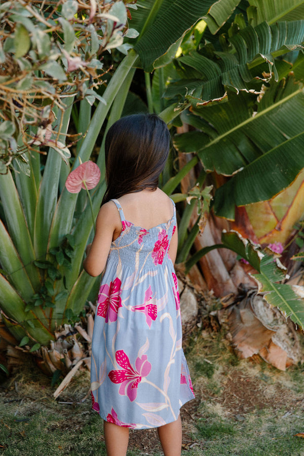 Girl wearing sleeveless dress with large pink floral print on lavender ground.