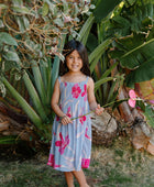 Girl wearing sleeveless dress with large pink floral print on lavender ground.