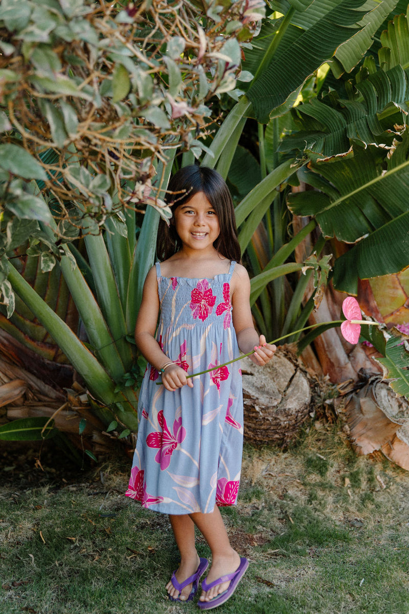 Girl wearing sleeveless dress with large pink floral print on lavender ground.