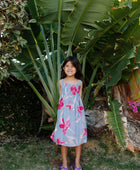 Girl wearing sleeveless dress with large pink floral print on lavender ground.