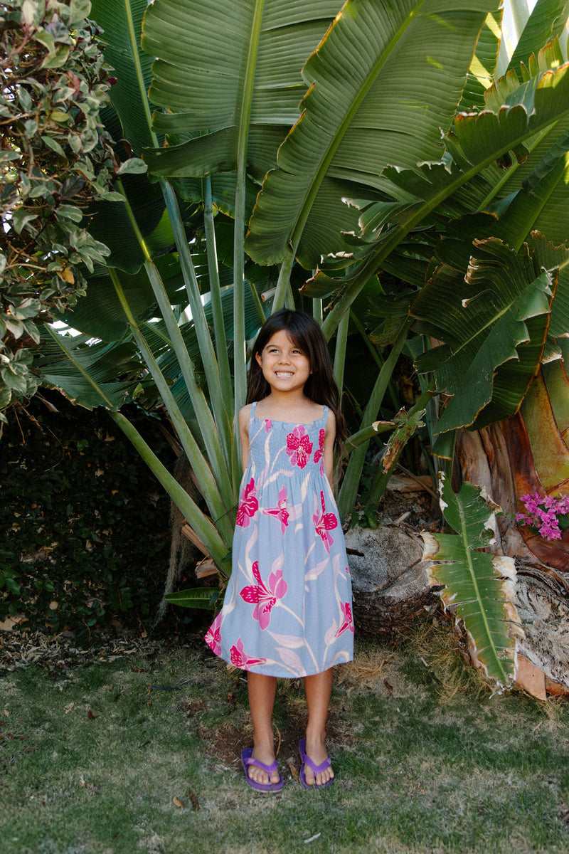 Girl wearing sleeveless dress with large pink floral print on lavender ground.