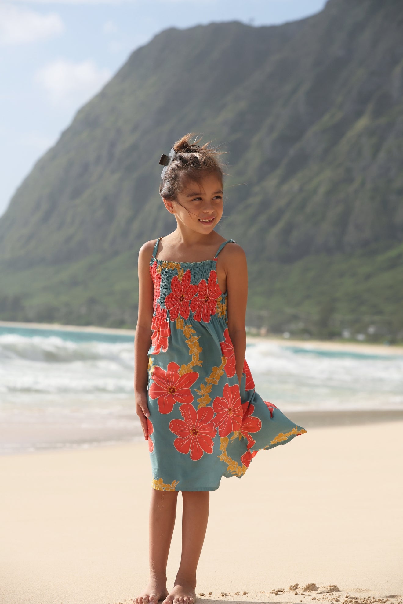 little girl wearing a green knee length dress with orange and yellow lei pua print 