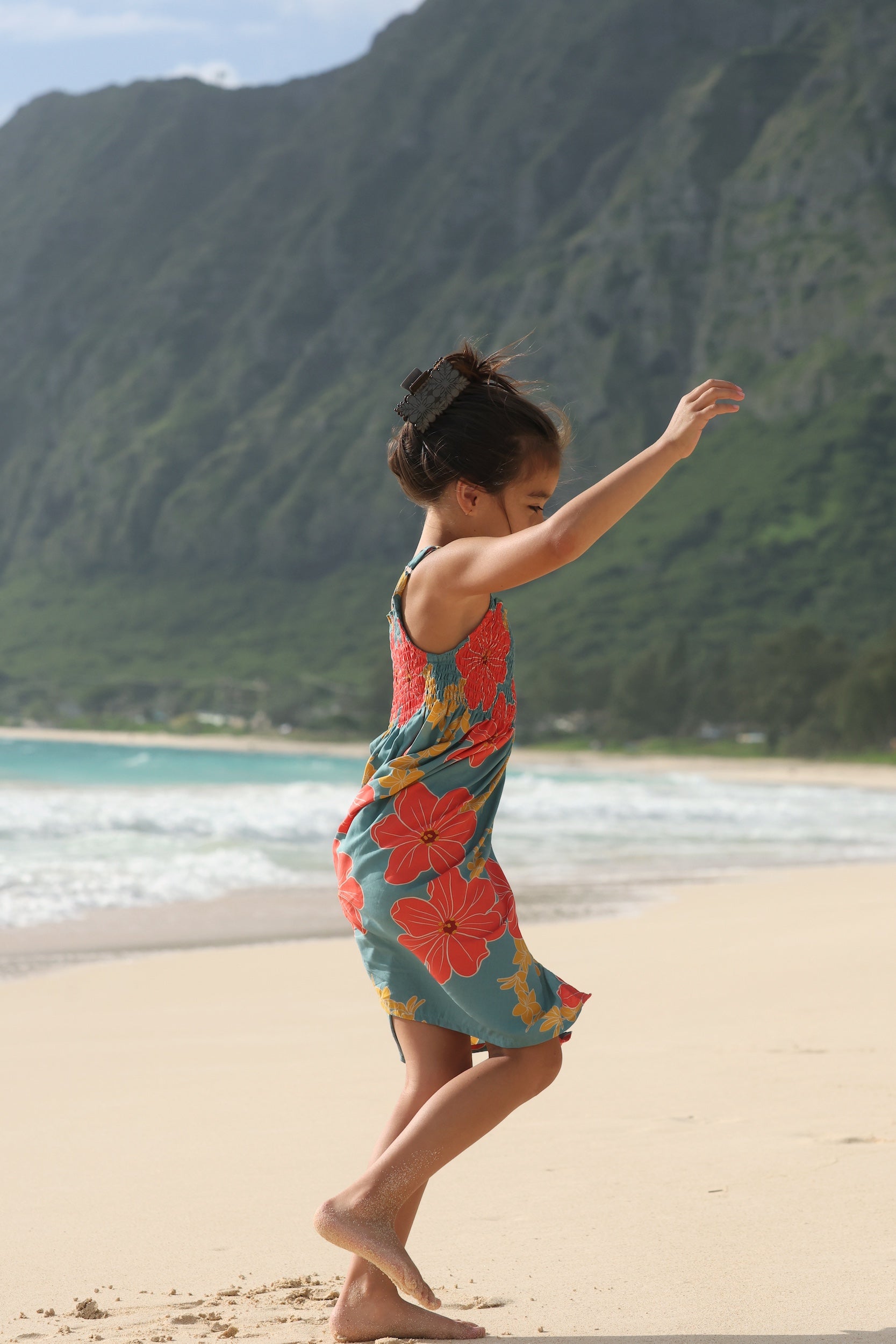 little girl wearing a green knee length dress with orange and yellow lei pua print 