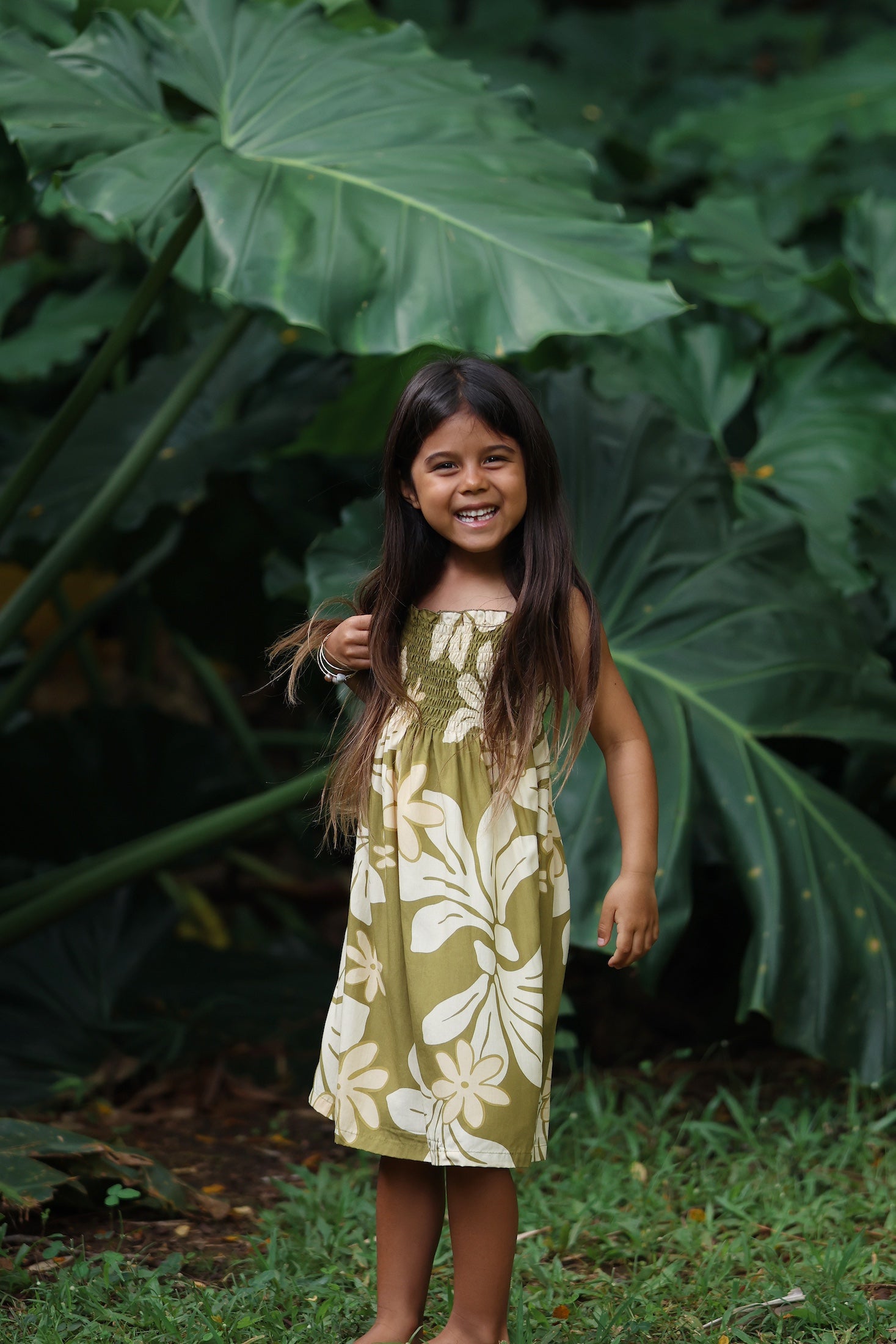 little girl wearing spaghetti strap dress in green print with naupaka pattern
