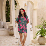 woman with brown hair wearing a dark green button-up, oversized shirt dress with fern and ginger print