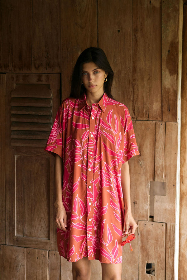 A woman with dark hair wears a YIREH collared, button-up dress. It is the Kaimana Dress in the Garden 'Awapuhi print. 