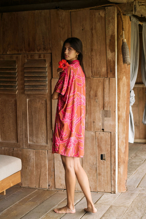 A woman with dark hair wears a YIREH collared, button-up dress. It is the Kaimana Dress in the Garden 'Awapuhi print. 