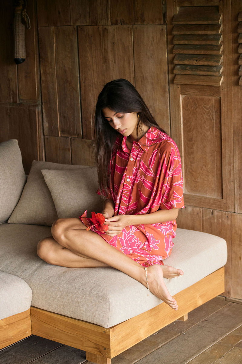 A woman with dark hair wears a YIREH collared, button-up dress. It is the Kaimana Dress in the Garden 'Awapuhi print. 