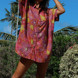 woman wearing terracotta colored button up shirt dress with large purple and yellow flower pattern