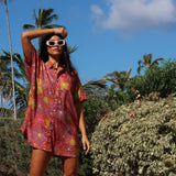woman wearing terracotta colored button up shirt dress with large purple and yellow flower pattern