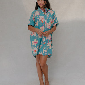 woman with brown hair wearing a teal button up collared dress with white orchid print