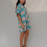 woman with brown hair wearing a teal button up collared dress with white orchid print