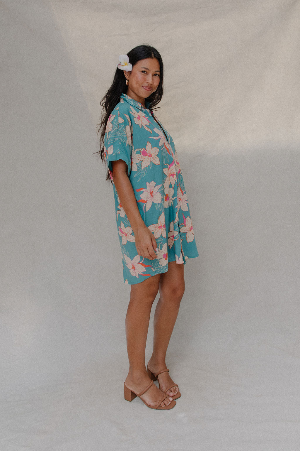 woman with brown hair wearing a teal button up collared dress with white orchid print