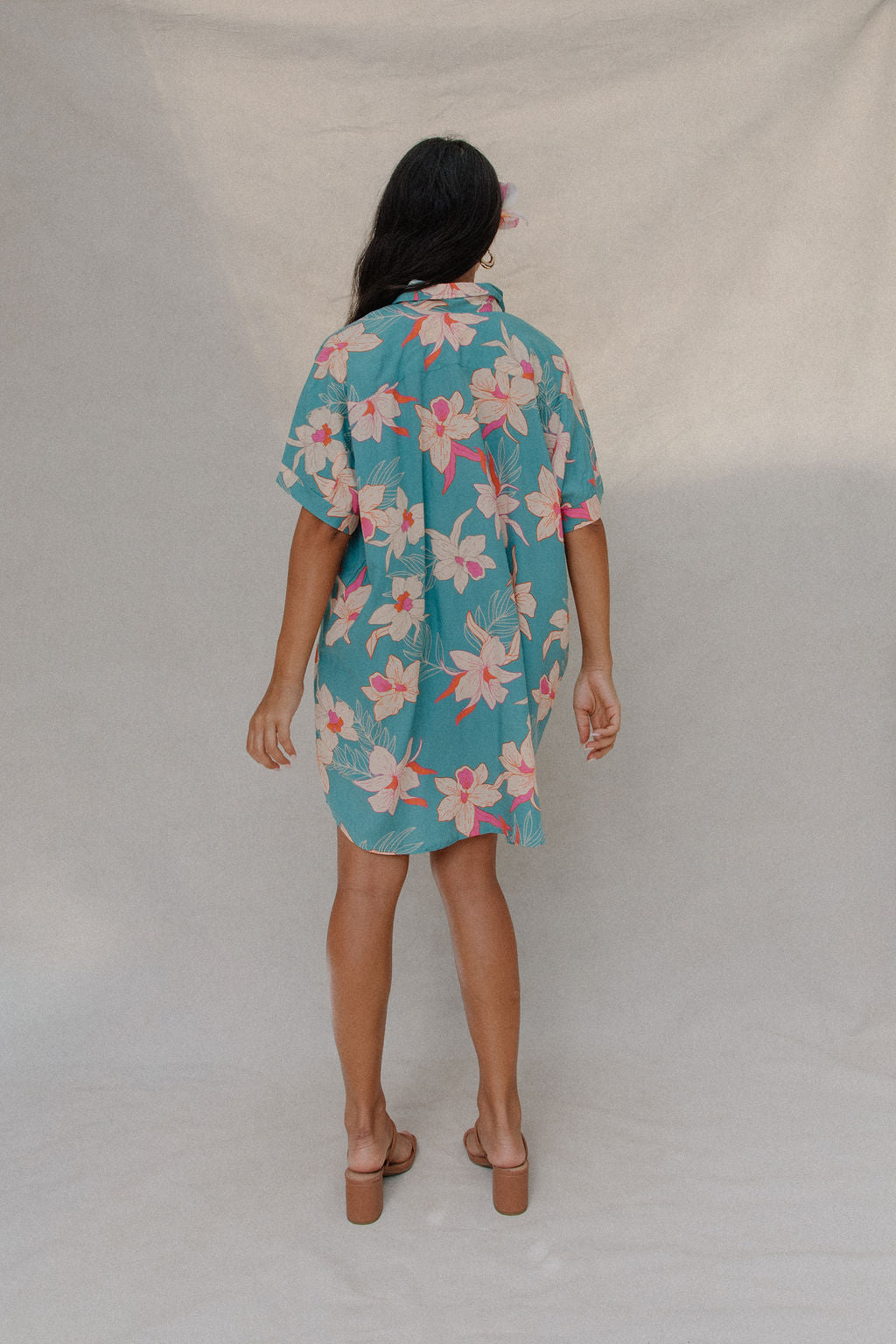 woman with brown hair wearing a teal button up collared dress with white orchid print
