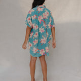 woman with brown hair wearing a teal button up collared dress with white orchid print