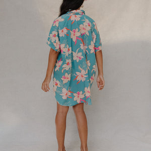 woman with brown hair wearing a teal button up collared dress with white orchid print