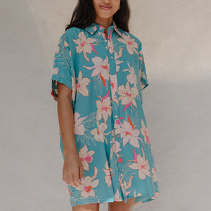 woman with brown hair wearing a teal button up collared dress with white orchid print