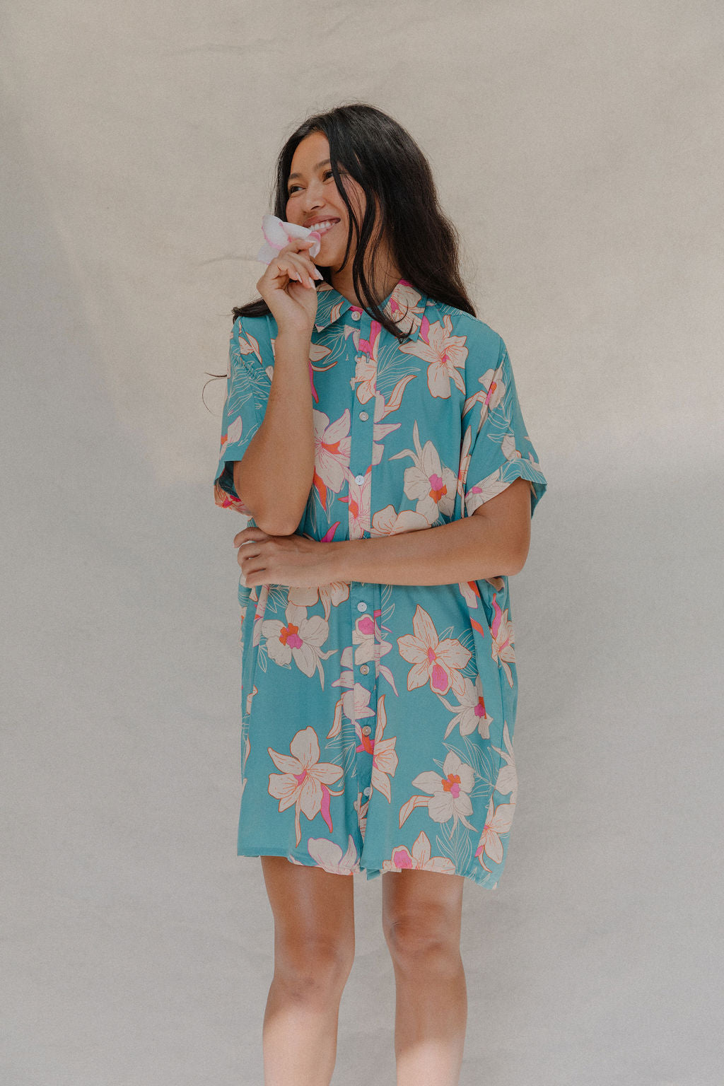 woman with brown hair wearing a teal button up collared dress with white orchid print