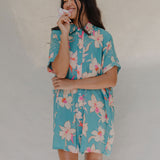 woman with brown hair wearing a teal button up collared dress with white orchid print