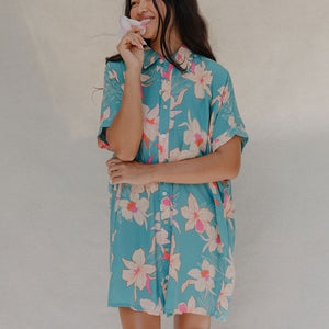 woman with brown hair wearing a teal button up collared dress with white orchid print