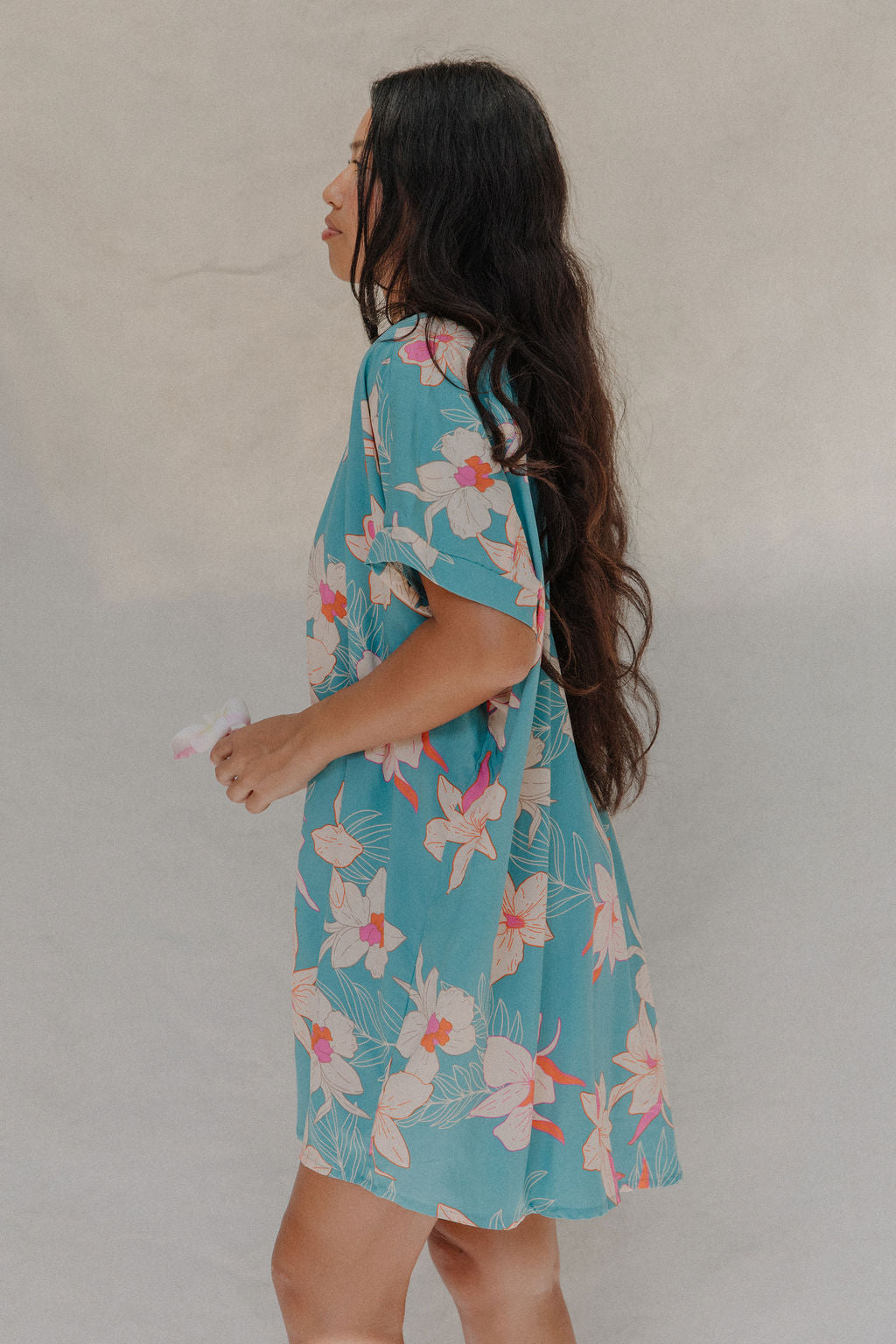woman with brown hair wearing a teal button up collared dress with white orchid print