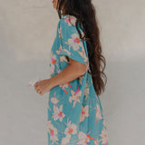 woman with brown hair wearing a teal button up collared dress with white orchid print