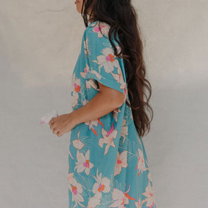 woman with brown hair wearing a teal button up collared dress with white orchid print