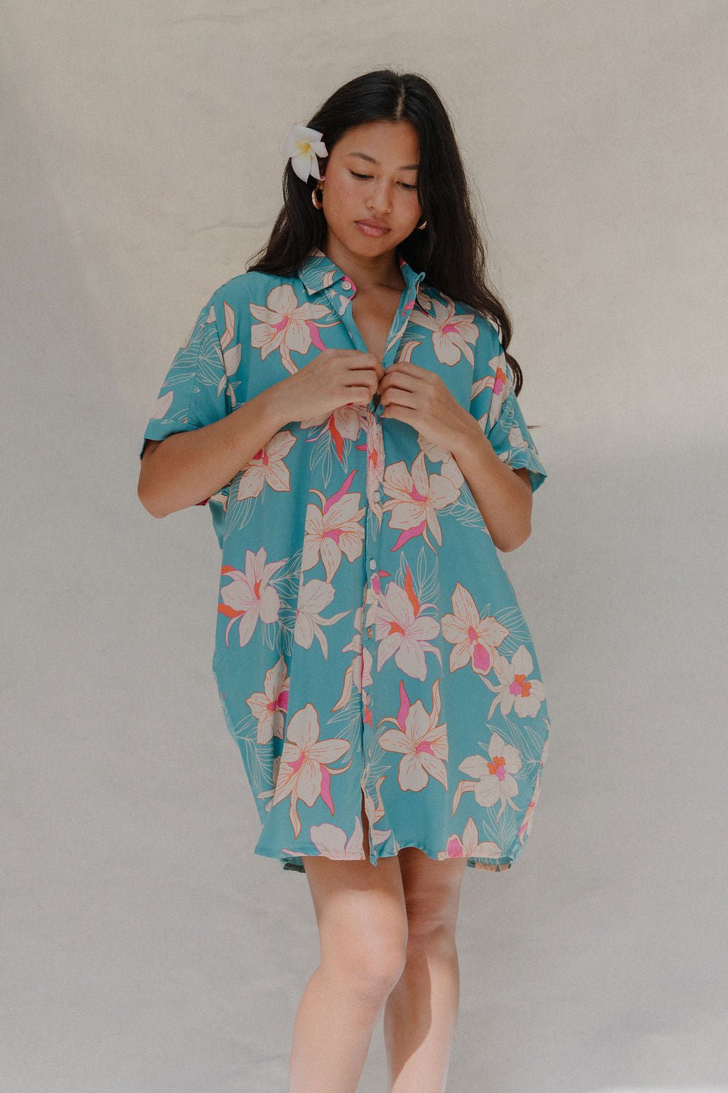 woman with brown hair wearing a teal button up collared dress with white orchid print