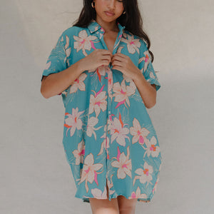 woman with brown hair wearing a teal button up collared dress with white orchid print