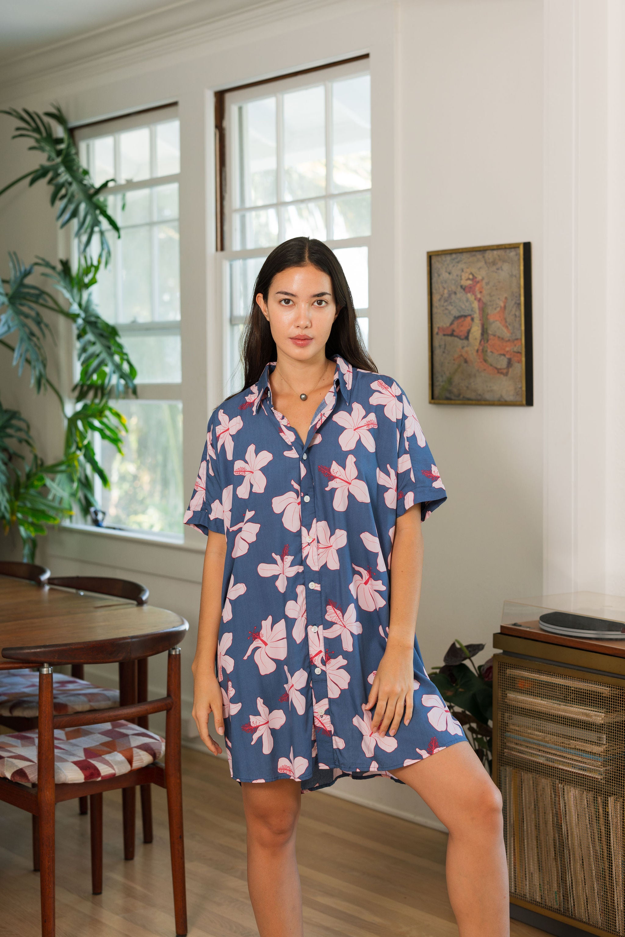 woman with black hair wearing a button up dress in a navy color with pink hibiscus blossoms 
