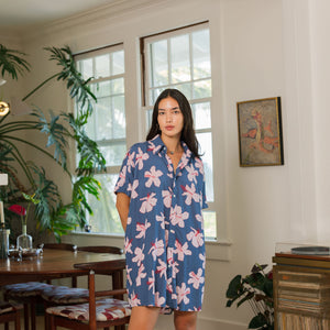 woman with black hair wearing a button up dress in a navy color with pink hibiscus blossoms 