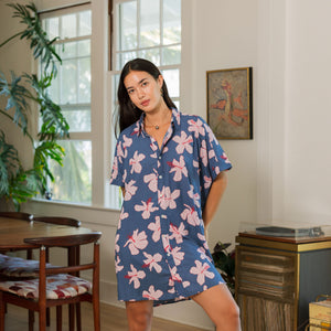 woman with black hair wearing a button up dress in a navy color with pink hibiscus blossoms 