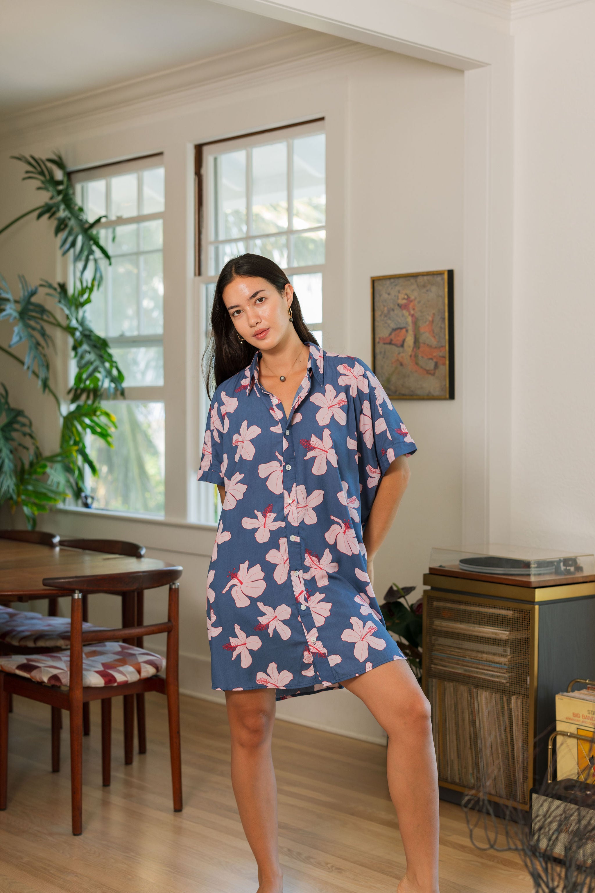 woman with black hair wearing a button up dress in a navy color with pink hibiscus blossoms 
