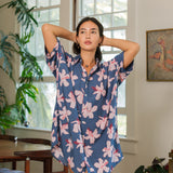 woman with black hair wearing a button up dress in a navy color with pink hibiscus blossoms 