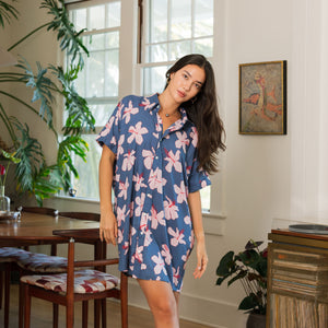 woman with black hair wearing a button up dress in a navy color with pink hibiscus blossoms 