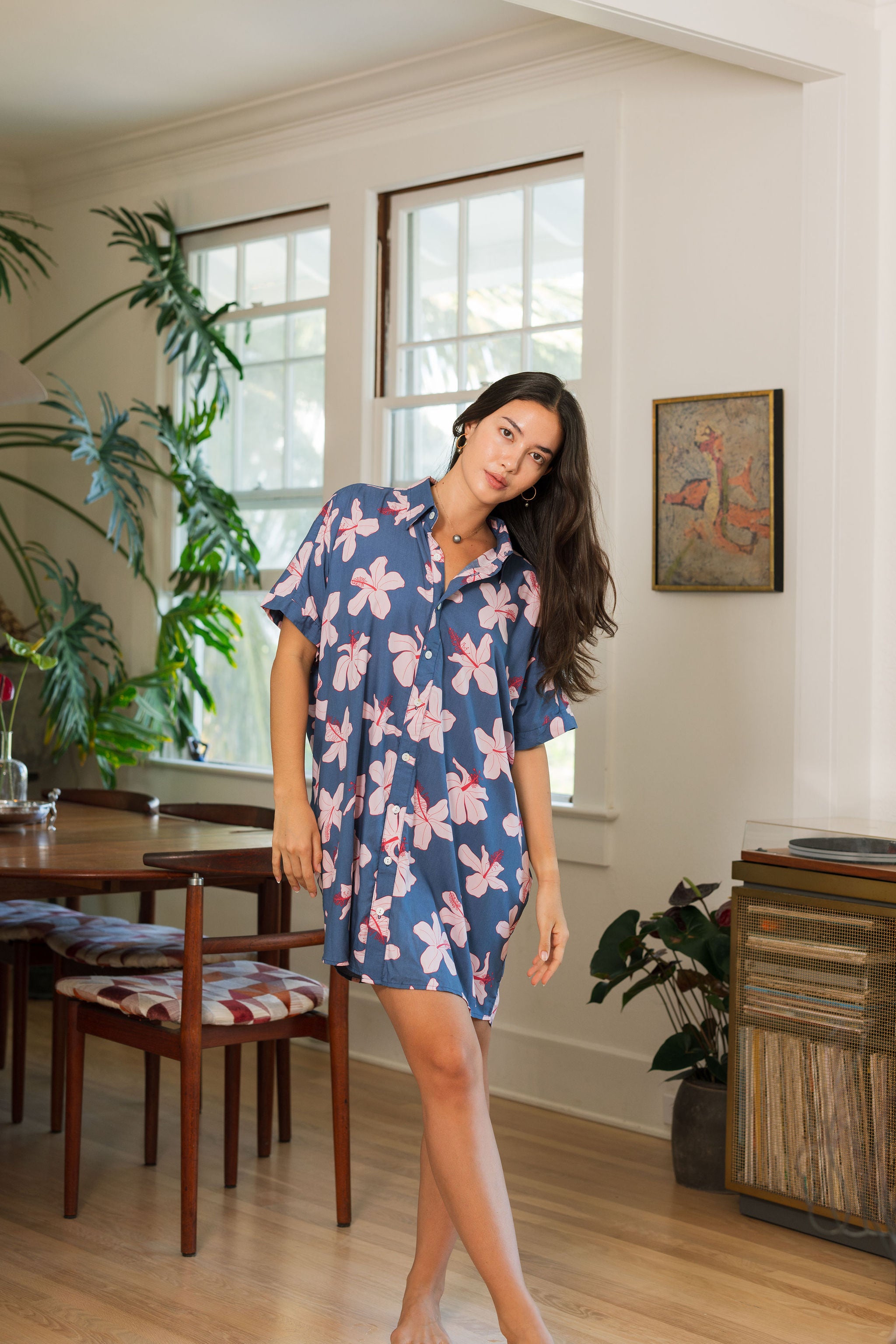 woman with black hair wearing a button up dress in a navy color with pink hibiscus blossoms 