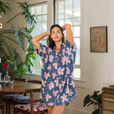 woman with black hair wearing a button up dress in a navy color with pink hibiscus blossoms 