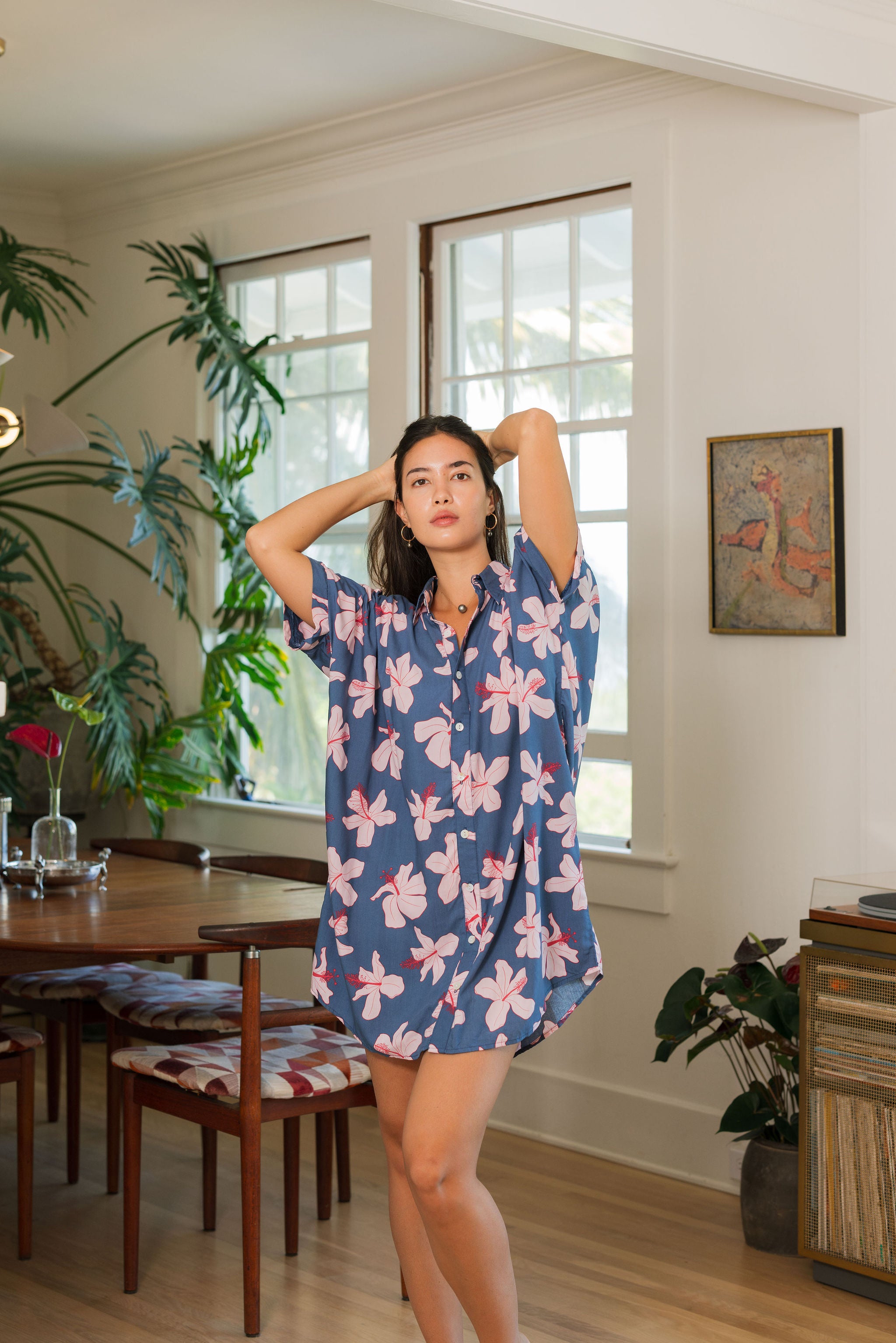 woman with black hair wearing a button up dress in a navy color with pink hibiscus blossoms 