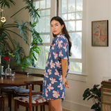 woman with black hair wearing a button up dress in a navy color with pink hibiscus blossoms 