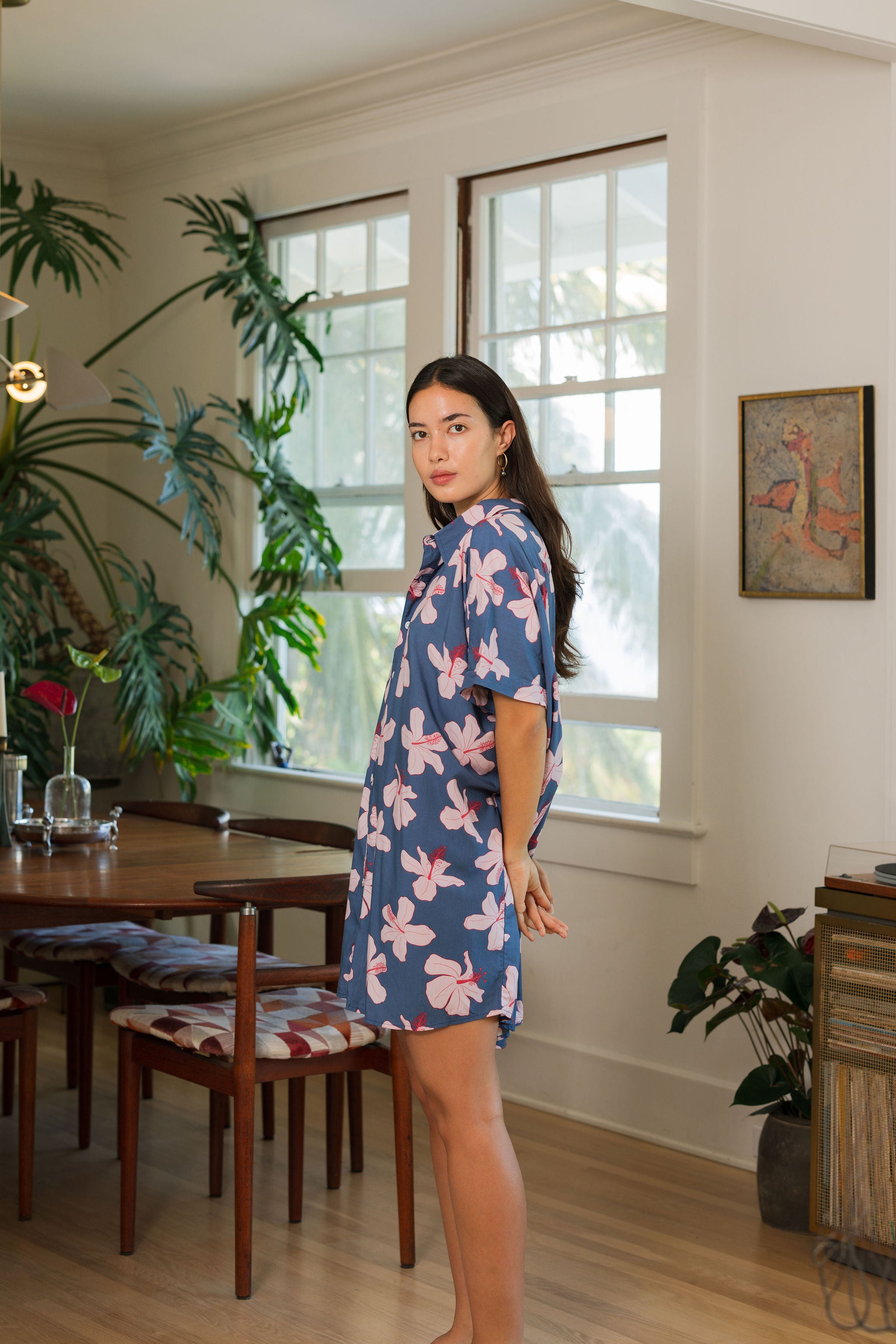 woman with black hair wearing a button up dress in a navy color with pink hibiscus blossoms 