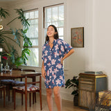 woman with black hair wearing a button up dress in a navy color with pink hibiscus blossoms 