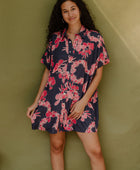 Woman wearing short sleeve shirt dress with pink floral print on dark navy ground.