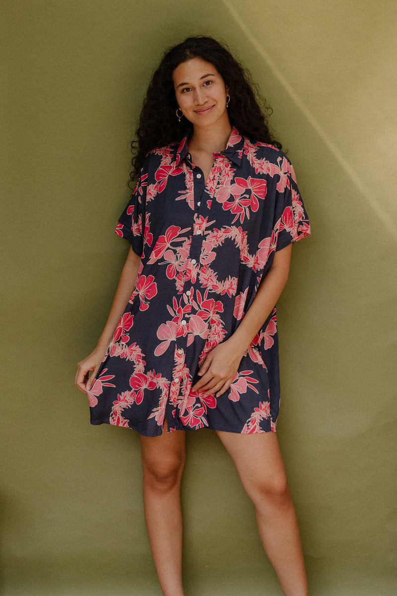 Woman wearing short sleeve shirt dress with pink floral print on dark navy ground.