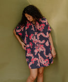 Woman wearing short sleeve shirt dress with pink floral print on dark navy ground.